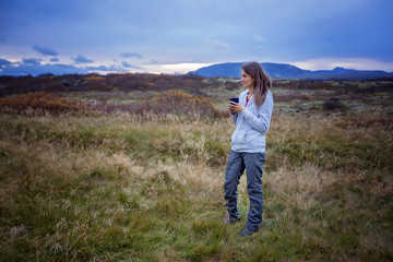Fototapeta premium Young woman, drinking coffee or tea, early in the morning in camping, enjoying the beautiful autumn view