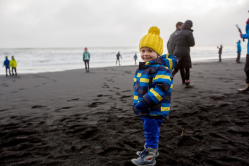 Toddler playin on black sand beach of Reynisfjara and the mount Reynisfjall in Iceland on a cold winter day