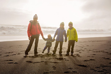 Family posing against the sun in black sand beach of Reynisfjara and the mount Reynisfjall in...