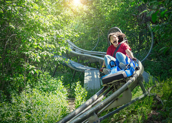 Screaming teen girl riding downhill on an outdoor roller coaster on a warm summer day. She has a...