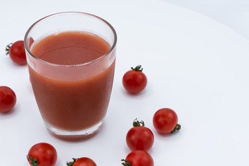 Glass of fresh organic tomato juice with raw tomatoes on white plate.