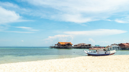 Obraz premium Beautiful view of crystal clear water, white sand, blue sky, traditional cottage, and wooden boat at Derawan Island, Indonesia