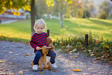 Beautiful blonde two years old toddler boy, riding red tricycle in the park on sunset