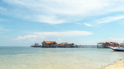 Beautiful view of crystal clear water, white sand, blue sky, traditional cottage, and wooden boat at Derawan Island, Indonesia