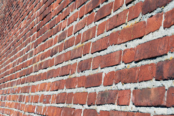 Large red brick wall. Side view. Perspective. The surface of the wall is slightly curved. Brickwork of a large number of bricks. Seams from a thick layer of cement mortar.