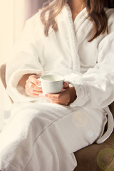 A girl in a white coat is drinking morning coffee.