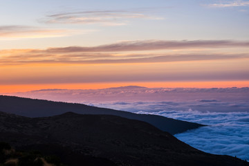Fototapeta na wymiar Sunset or sunrise beautiful landscape moment at the mountain - high peak vulcan and coloured sunlight in background - blue sea of clouds - beauty of outdoor nature