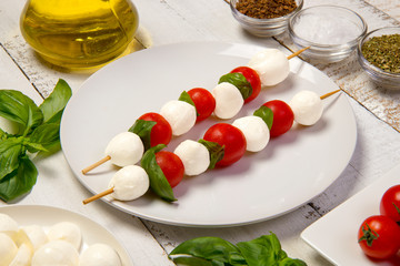 Traditional caprese salad on a white wooden table with ingredients. Selected focus.