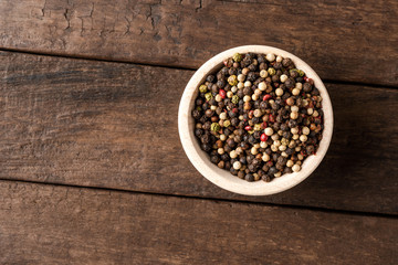 Fototapeta na wymiar Mixed peppercorns in bowl on wooden table. Close up. Top view