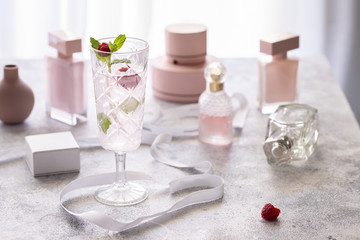 Fototapeta na wymiar Pink fresh cocktail with raspberry and mint on table with rose bottle perfume bottle. Concept for female drink.