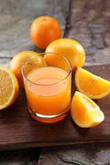 Orange Juice glass on a stone background along with the fresh fruit pieces.