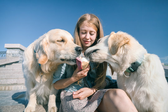 A young girl feeds her dogs ice cream in a park on a hot summer day.