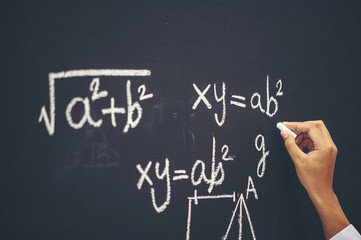 The hand that writes the formula with white chalk on the blackboard