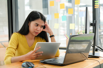 Female programmer are using tablet to create programs for clients. She put hand on temple and face was serious.