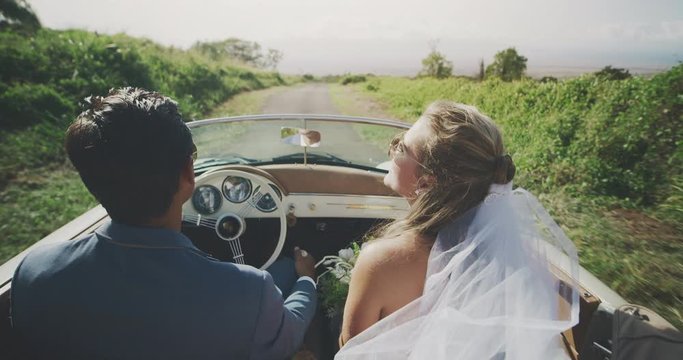 Happy diverse newly wed couple driving on a country road, bride and groom driving together in a vintage convertible
