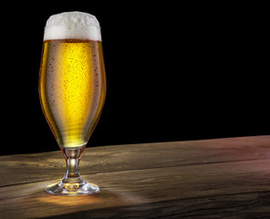 Glass of light beer on the bar counter on a black background.