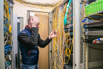 A sad specialist took up his head at the sight of problems with wiring in the server room. Facepalm technician. Incorrect connection of communication equipment in the data center.