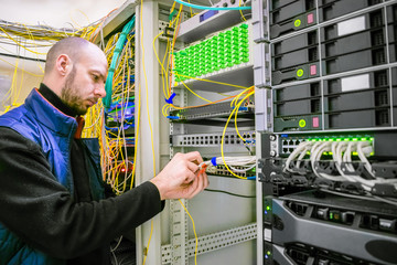  A man commutes Internet wires in a server rack. The system administrator works in the server room...