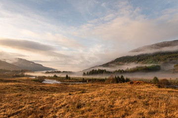 Sun is setting as low hanging clouds run through the River Orchy, a pine forest and the hills in the distance on a partially cloudy day in the Highlands of Scotland.,Blue, Brown, Clouds, Color, Colour