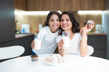 beautiful young mother with her cute teenager daughter eating cupcakes and croissants and drinking...