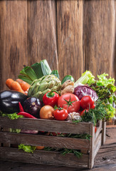 Fresh multi-colored vegetables in wooden crate. Wooden background.