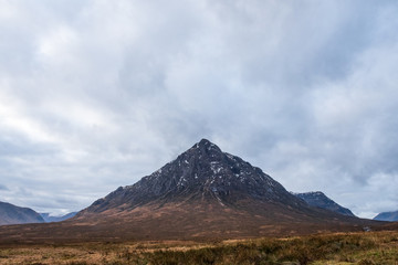 Fototapeta premium Wintery brown grass fields overlooks Buachaille Etive Mòr mountain on a cloudy day in the Scottish Highlands.