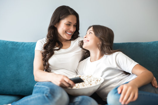 beautiful young mother with her cute teenager daughter watching movie on the sofa eating popcorn feeling comfortable at home