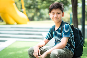 A smart looking preteen student boy siting outdoor under the tree shade in front of the school. Back to school, Preteen, Tween, Education, Friendly, Healthy, Growing up concept.