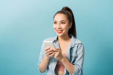 Fototapeta premium Portrait of a cheerful casual girl holding mobile phone over blue background