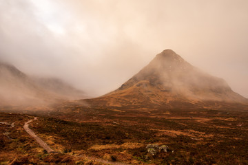 Fototapeta premium Wintery brown grass fields overlooks low-hanging clouds that cover Bidean Nam Bian mountain covered in clouds in the Scottish Highlands.