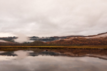 Calm waters at Loch Eil with a view of the wintery and brown Scottish Highlands on cloudy day.