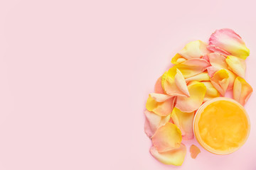 Open jar of cosmetic cream and rose petals on pink background. Concept of organic spa cosmetics. Flat lay, top view, copy space.	