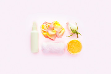 Open jar of cosmetic cream, white cosmetics bottle, towel and rose on pink background. Concept of natural spa cosmetics. Flat lay, top view, copy space.