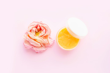 Open jar of cosmetic cream and rose on pink background. Concept of organic spa cosmetics. Flat lay, top view, copy space