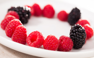 raspberries and blackberries laid out on a white plate in circle