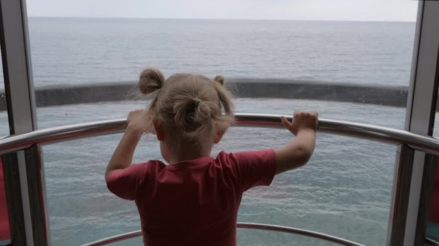 A little girl goes up in a transparent Elevator overlooking the sea.