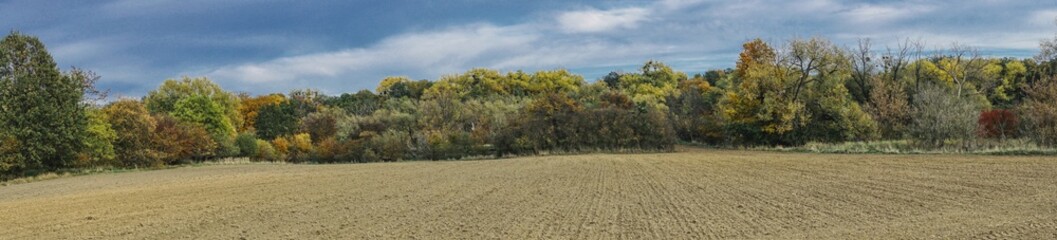 rural panorama of a plowed field and colorful autumn forests