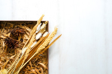 Flat lay composition for autumn holidays greeting cards. Pine cones, wheak, leaves, flowers in a wooden box on the wooden background. Top view, copy space.