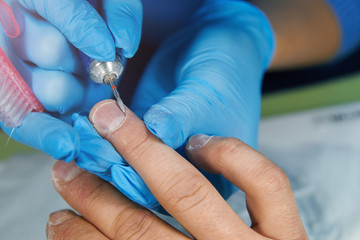 Man in blue gloves manicures nails with a mill on a male hand