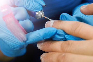 Man in blue gloves manicures nails with a mill on a male hand