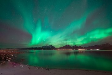 Aurora covering the sky above mountain range. In foreground sand beach. Northern lights reflects in the ocean.
