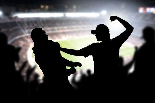 Fight in a football game crowd. Angry man hitting another spectator in soccer match audience. Violent argument between two fans of different teams and clubs. Hooligans and violence in sport event.