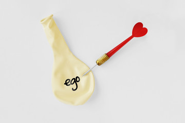 Deflated balloon with the word ego on it and arrow dart with heart on white background - Ego and love concept - obrazy, fototapety, plakaty