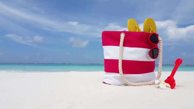 close up shot of pink white striped beach bag, sunglasses flip-flops plastic shovel and frangipani flower, family vacation background