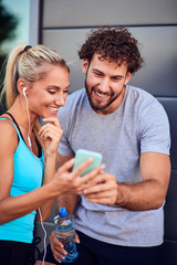 Modern woman and man jogging / exercising in urban surroundings and using cellphone at a pause / break.