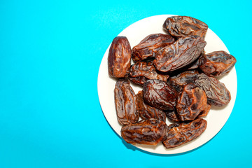 Fresh arabic dates isolated in white plate on blue background with copy space. Top view. Date palm fruit.