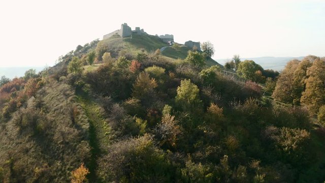 Flight above abandoned ruined Branc castle on a hill above a village near an autumn forest, Slovakia.