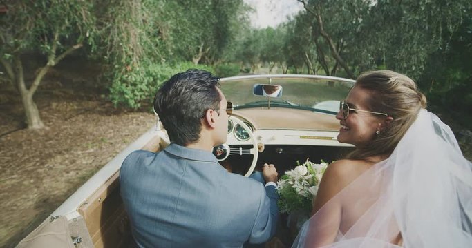 Happy smiling diverse newly wed couple driving on a country road, bride and groom driving together in a vintage convertible