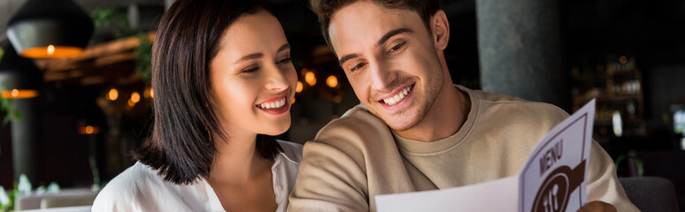 panoramic shot of happy man and woman looking at menu