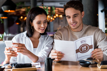 happy woman holding smartphone near man with menu